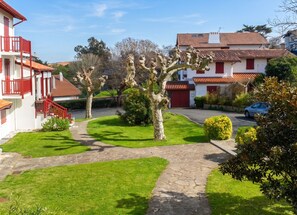 Un quartier résidentiel avec un chemin pavé, une pelouse bordée d’arbres et une voiture garée.