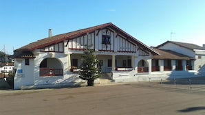 Un bâtiment à deux étages, doté d’une façade blanche et de touches de couleur rouge, avec un balcon et un petit arbre devant.