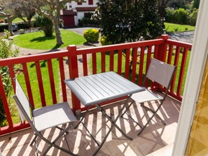 Un balcon avec une balustrade rouge, une table grise et deux chaises blanches.