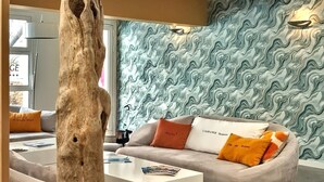 A modern living room with a unique tree sculpture centerpiece, a sofa with colorful cushions, and a patterned wall.
