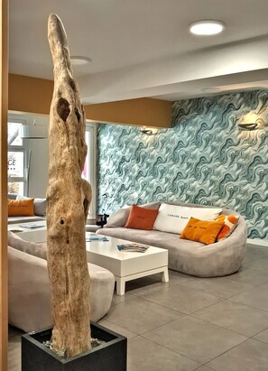 A modern living room with a unique tree sculpture centerpiece, a sofa with colorful cushions, and a patterned wall.