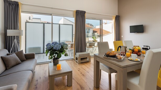 A modern living room with a sofa, a coffee table with a candle, and a dining area with breakfast items.