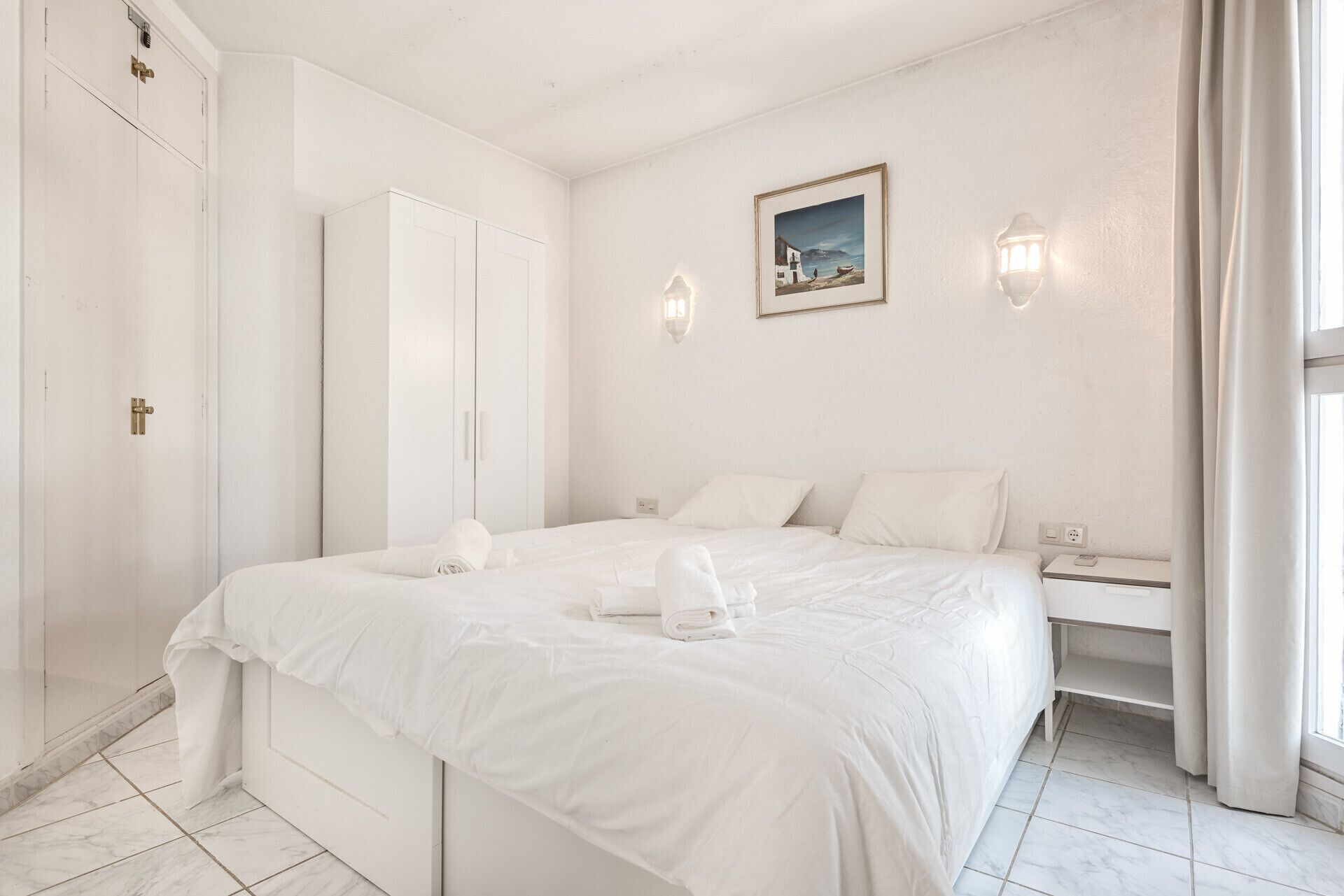A bedroom with a large bed, a wardrobe, a desk, and a painting on the wall.
