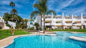 Una piscina con acqua cristallina, circondata da un edificio bianco con balconi e palme.