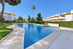 A swimming pool with a curved edge, surrounded by a well-maintained lawn and a row of white buildings with yellow accents.
