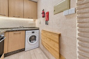 Una cocina compacta con lavadora, armarios de madera, salpicadero de azulejos y extintor.