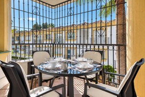 A balcony with a table set for four, surrounded by chairs, overlooking a residential area with yellow buildings.