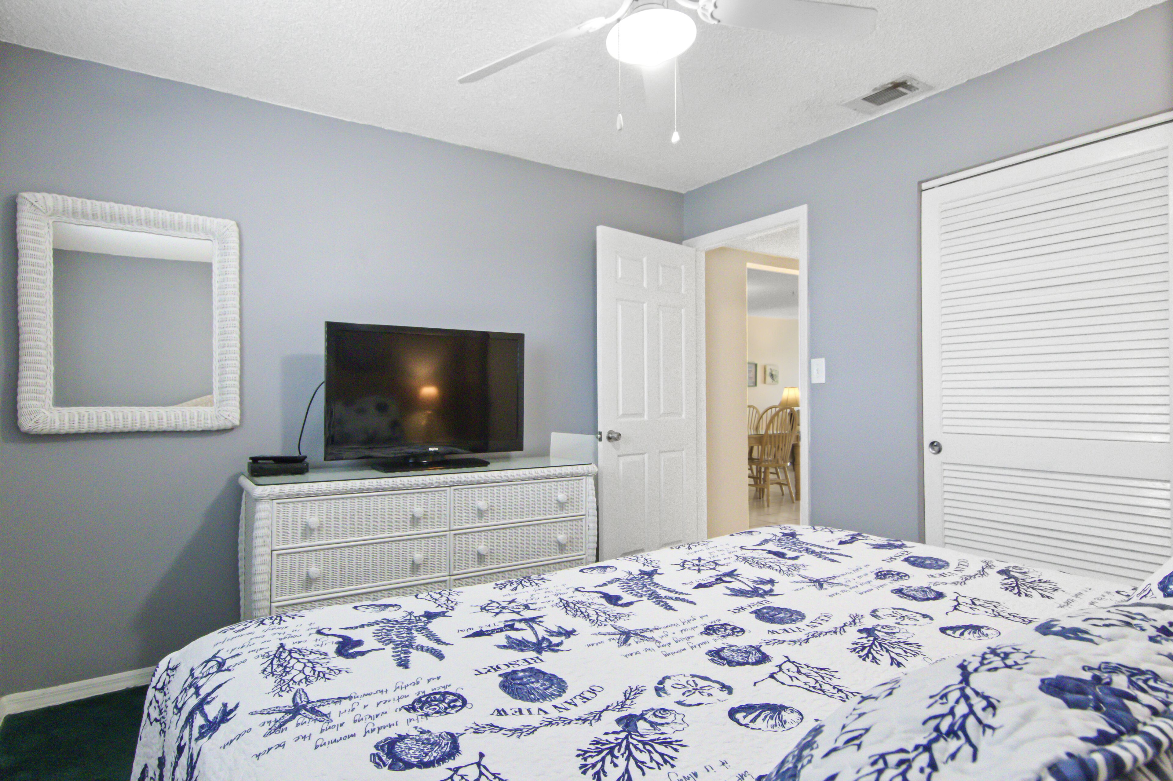 Un dormitorio con cama, cómoda, televisor y una puerta que da a otra habitación.