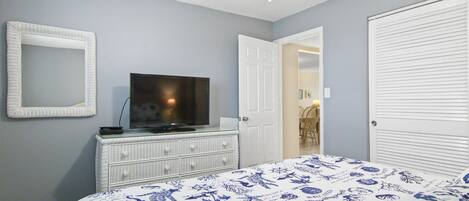 Un dormitorio con cama, cómoda, televisor y una puerta que da a otra habitación.