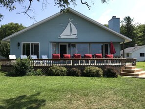 Une maison bleue avec un logo représentant un voilier sur la façade, une véranda avec des coussins rouges et une cour verdoyante.