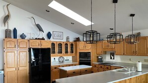 A modern kitchen with wooden cabinets, a black refrigerator, a stainless steel stove, and a large island with bar stools. - Waterfront Vacation Home Directly on Hubbard Lake - East Shore (Spruce)