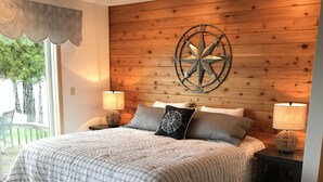 A bedroom with a large bed, wooden panel walls, a compass wall decoration, and two bedside lamps. - Waterfront Vacation Home Directly on Hubbard Lake - East Shore (Spruce)