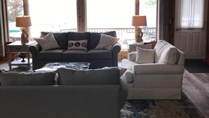 A cozy living room with a ceiling fan, two couches, and a coffee table. Large windows allow natural light and provide a view of the outdoors. - Waterfront Vacation Home Directly on Hubbard Lake - East Shore (Spruce)