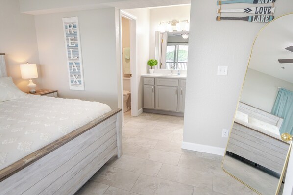 Un dormitorio con cama, mesita de noche, espejo en la pared y baño con lavabo y armarios.