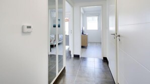 A hallway with a sliding door leading to a bedroom, a thermostat on the wall, and a window at the end.