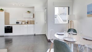 A modern kitchen with white cabinets, a dining area with a table set for two, and a view of a staircase and building outside the window.