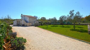 A stone building with a red-tiled roof, a gravel driveway, and a grassy area with trees. - Bavica studio with private parking (Rovinj)