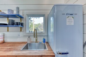 Una cocina con un lavamanos de acero inoxidable, un refrigerador azul y estantes con platos y tazas.