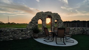 Une construction en pierre dotée de fenêtres en arc de cercle et d’une table entourée de chaises, le tout situé dans un jardin.