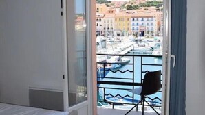 Ein Zimmer mit einem Bett, einer Glastür zu einem Balkon mit einem Stuhl und Blick auf eine Marina.