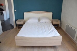 A bed with a wooden frame and white bedding, two bedside tables, and a teal wall.
