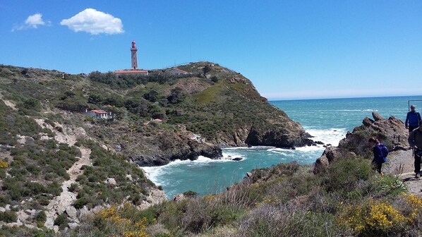 Un paisaje costero con un faro en una colina, terreno rocoso y una vista despejada del mar.