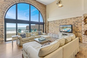 Relax in this beachside living room with a sofa, chairs, and flat-screen TV, offering a view of the ocean.