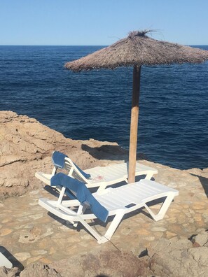 A beachside lounge with two white lounge chairs and a thatched umbrella, overlooking the sea. - Cap Sa Sal - Sa Roca 1 (Begur)
