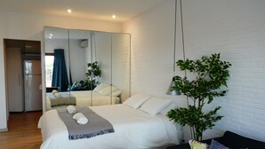 Une chambre moderne avec un grand lit, un miroir, une plante et une petite table.