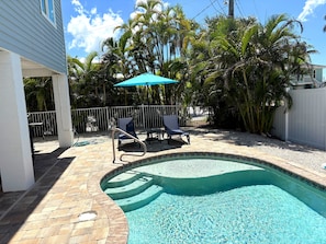 A backyard with a swimming pool, two lounge chairs, a patio table, and a white fence.