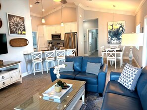 A modern living room with a blue sofa, white chairs, and a coffee table with a plant.