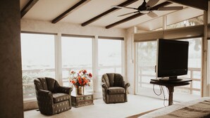 A spacious room with large windows, a ceiling fan, a flat-screen TV, and two leather armchairs.