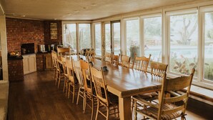 A spacious dining area with a long wooden table and chairs, a brick fireplace, and large windows offering a view of the outdoors.