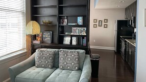 A living room with a light blue sofa, a dark wooden bookshelf, and a window with blinds.