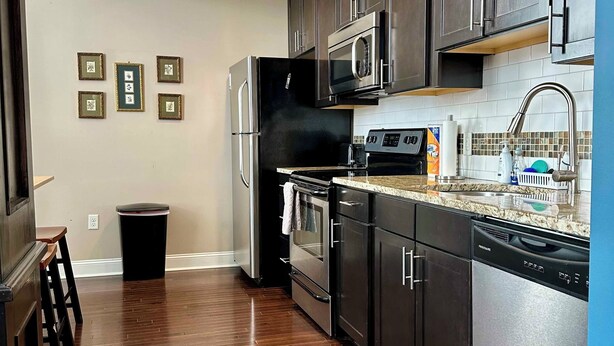 A modern kitchen with dark cabinetry, stainless steel appliances, and a tiled backsplash.