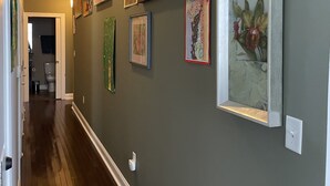 A hallway with wooden flooring, a green wall, and several framed artworks.