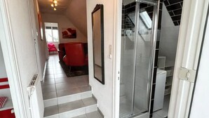 A hallway with a staircase leading to a room with a glass door, a red chair, and a framed picture on the wall. - Homerez - House in Cléder. (Cléder)