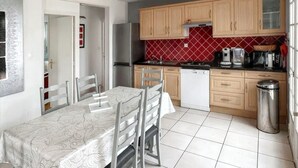 A modern kitchen with wooden cabinets, a dining table with chairs, and a tiled floor. - Homerez - House in Cléder. (Cléder)