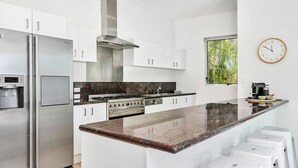 A modern kitchen with stainless steel appliances, a marble countertop, and a large window with a view of greenery.