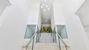 A modern staircase with glass railings and a view of greenery outside.
