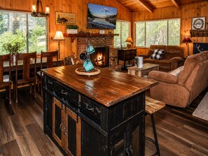 A cozy cabin interior with a wooden dining table, a fireplace, a sofa, and a large wooden cabinet.