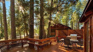 A wooden deck with a barbecue area, surrounded by tall trees.