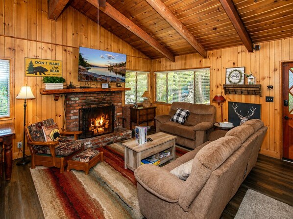 A cozy cabin interior with a fireplace, wooden walls, a sofa, and a television.