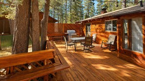 A cabin with a deck, outdoor seating, and a grill.