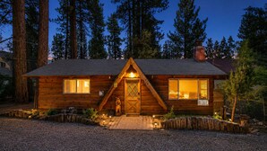 A wooden cabin with a triangular front, a chimney, and a lit entrance.