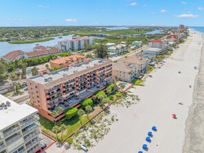 Un hotel frente al mar con varios balcones, piscina y playa con sombrillas.