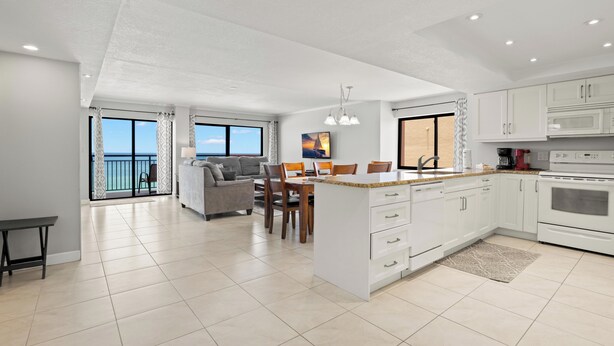A modern kitchen with white cabinets, a central island, and a dining area with a sofa and chairs.
