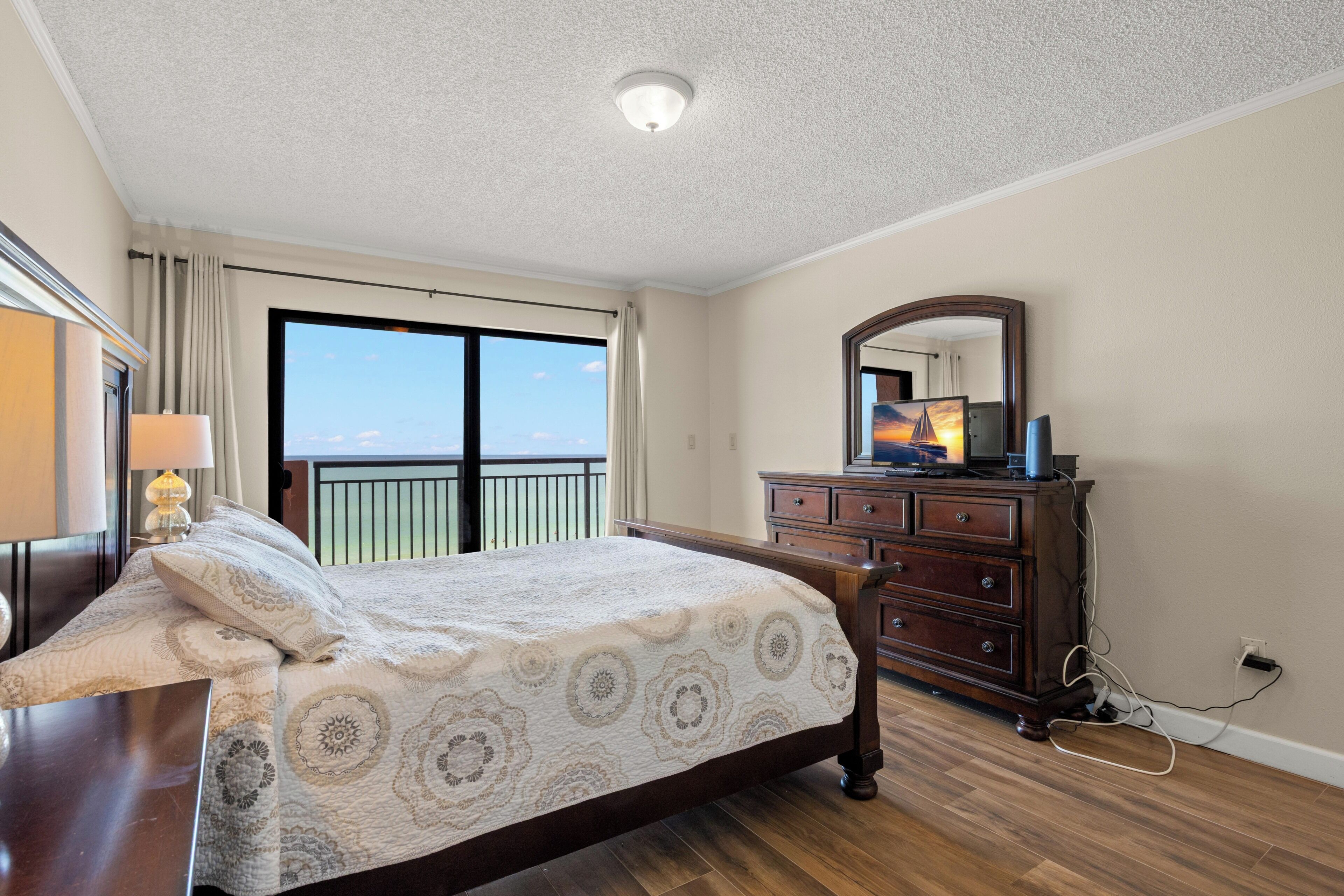 A bedroom with a bed, dresser, and a large window with a view.