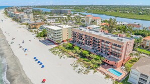 A beachfront hotel with multiple buildings, a swimming pool, and a beach with umbrellas.