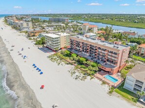 A beachfront hotel with multiple buildings, a swimming pool, and a beach with umbrellas.